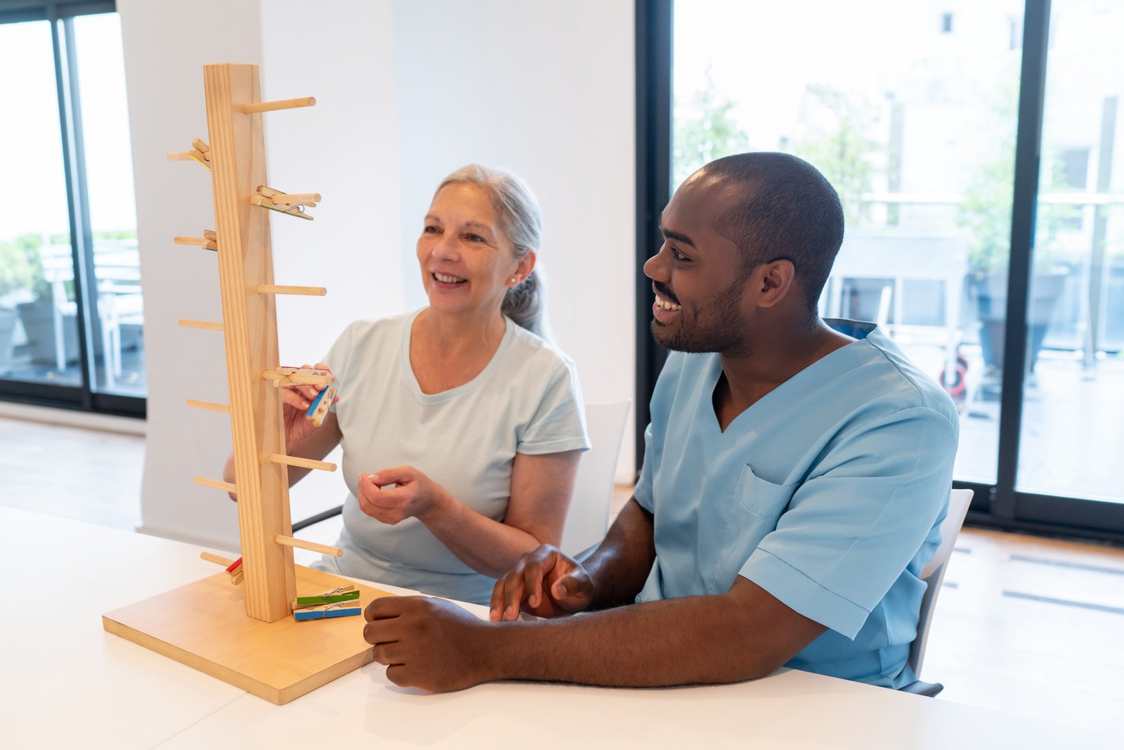 cheerful senior woman in occupational therapy with a black male patient having fun